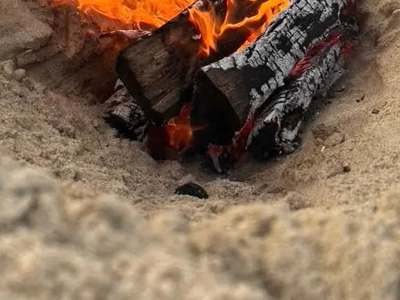 Logs burning in a small fire pit dug into beach sand