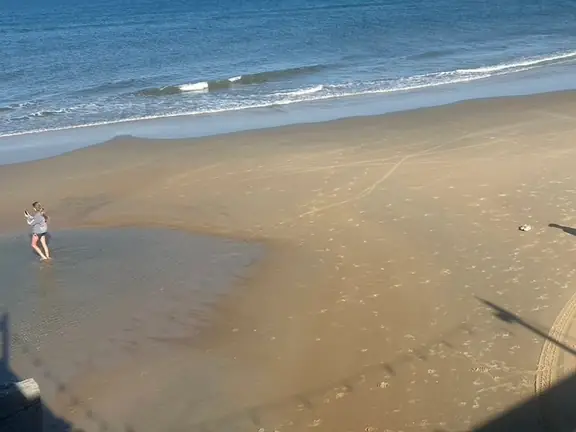 Two people walking at the water's edge, seen from a beach house deck above the sand